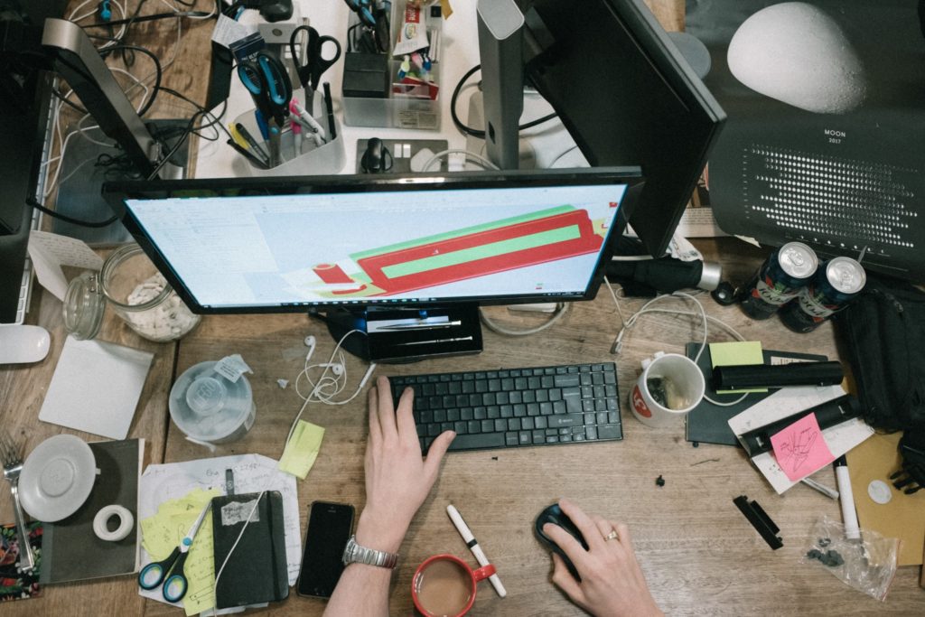 a person's hands on a desk with a computer and other objects