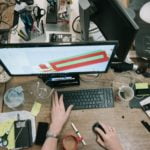 a person's hands on a desk with a computer and other objects